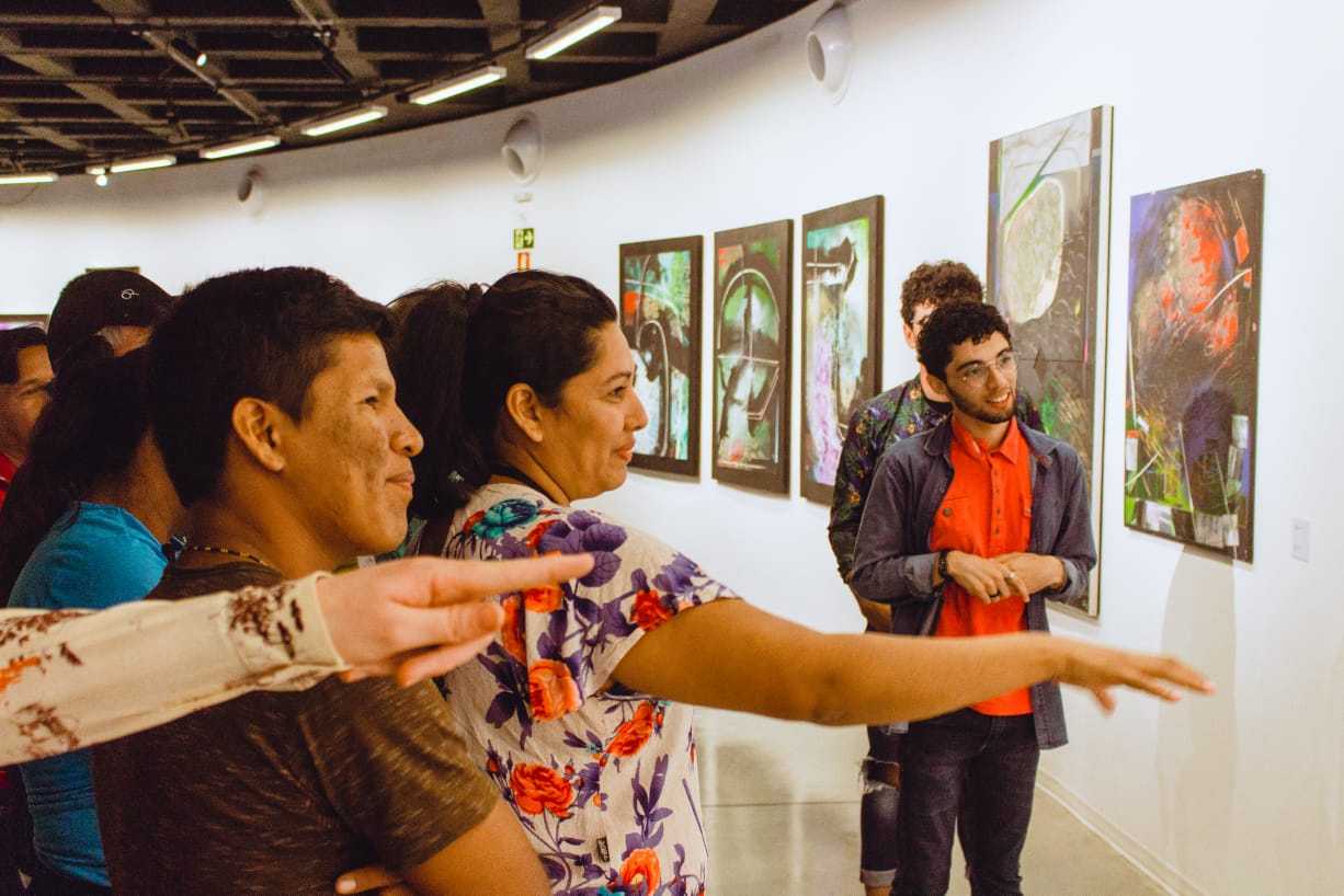 Tai conversando com os estudantes indígenas da Universidade Federal de Goiás (UFG) que foram visitar sua exposição. Estavam em frente às ilustrações científicas de araras e periquitos.
A filha de Tai, Lian, está com um bebê no colo. Ela é ativista dos direitos indígenas e por acaso foi ao encontro. Ao final, convidaram-a para visitá-los na UFG.
Exposição no Brasil com as mesmas obras que foram expostas na Expo China 2018. Foram exibidas no Museu de Arte Contemporânea de Goiânia (GO).
Entre as obras, apresentou desenhos, gravuras, instalações e esculturas também.