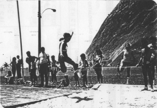 Maria Elizabeth realizando o salto que lhe garantiria o terceiro lugar na prova de salto em distância das olimpíadas do BNDES. Ao fundo estão Renata e Roberta (filhas de Maria Lúcia Andrade), Sandra Helena Siqueira, Márcio Lopes e Irani.