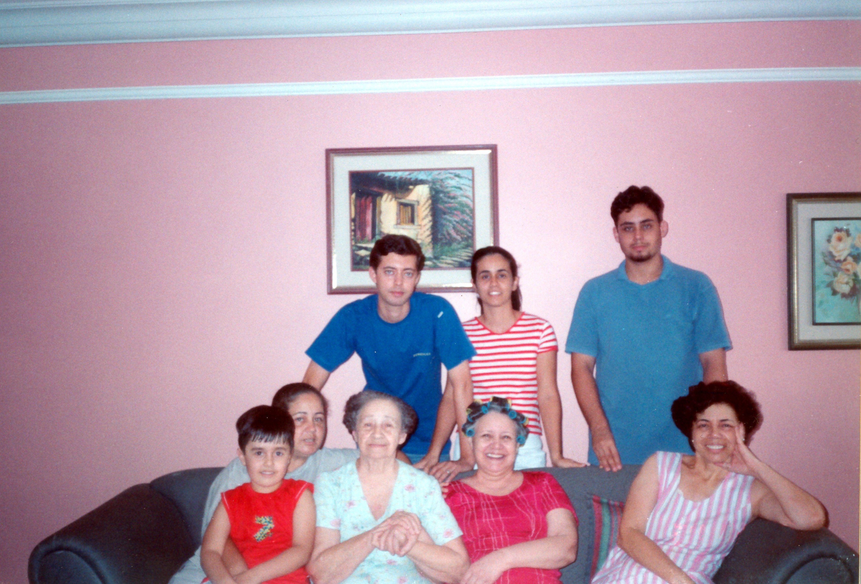 Retrato de Mirna e sua família no sofá. De pé, da esquerda para a direita: Flávio (sobrinho), Danielle (sobrinha e filha adotiva), João Paulo (sobrinho). Sentados: Jean (sobrinho e neto), Elizabeth (irmã), Diva (mãe), Olnei (irmã) e Mirna.