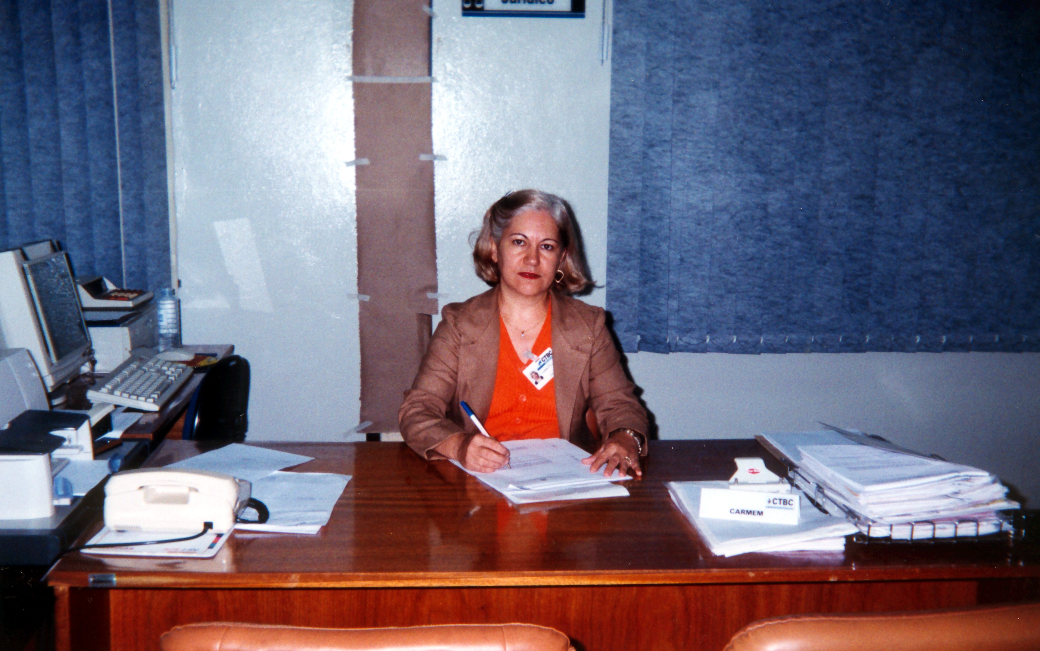 Carmen sentada atrás de sua mesa de trabalho na CTBC, onde ocupava o cargo de advogada há quatro anos. A amiga Nancy, com quem Carmen trabalhava junto há muito tempo, registrou o momento.