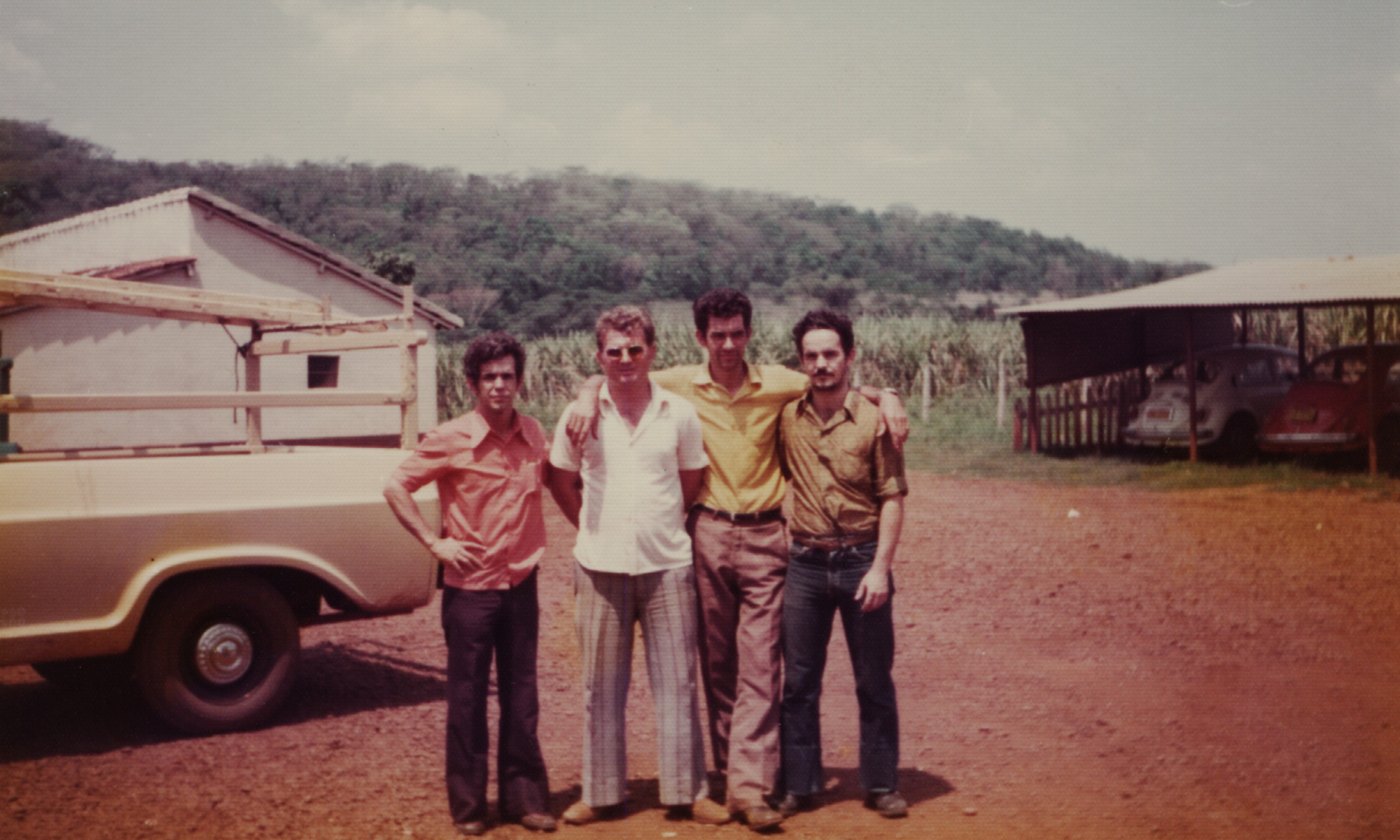 Dilson é o primeiro da esquerda para a direita. Ele e seus colegas estão de pé, ao lado uns dos outros, abraçados. O local é no pátio do estacionamento da CTBC. Estão presentes na foto, da esquerda para a direita: Dilson, Luiz, s. nome e Mário.