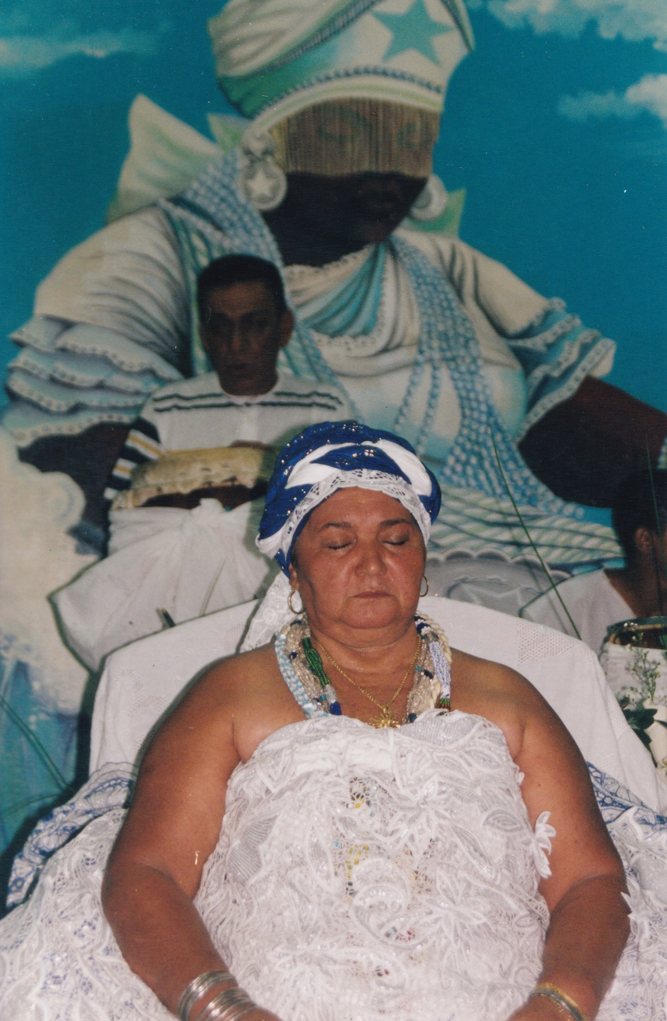 Mãe Néia de olhos fechados no barracão. Ao fundo, figura de Yemanjá pintada na parede