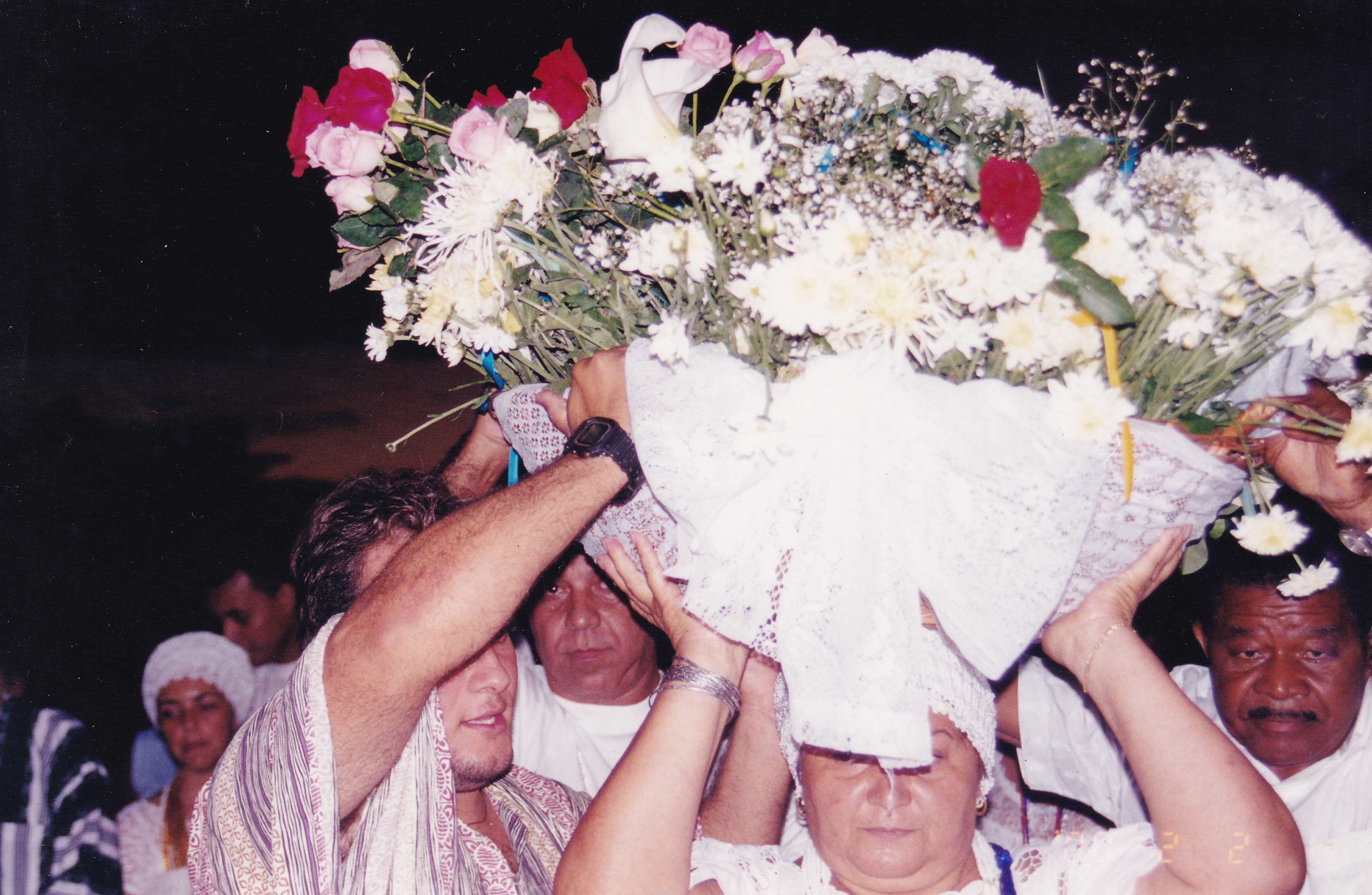 Mãe Néia e sacerdotes na festa de Yemanjá carregando balaio de flores ao anoitecer. Registro na Praia de Camburi, em Vitória?