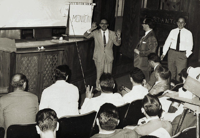 Oswaldo explica o Monicin, produto indicado para candidíase vaginal e micoses cutâneas, aos gerentes e supervisores da empresa. O evento foi realizado no auditório da Avenida do Estado e o produto foi veiculado até 1976. Em pé, da esquerda para a direita: Oswaldo Ruiz Urbano, José Augusto Pinto (gerente da divisão farmacêutica) e João Alfredo Mendes Filhos (gerente de produtos dos neurolépticos da linha Janssen).