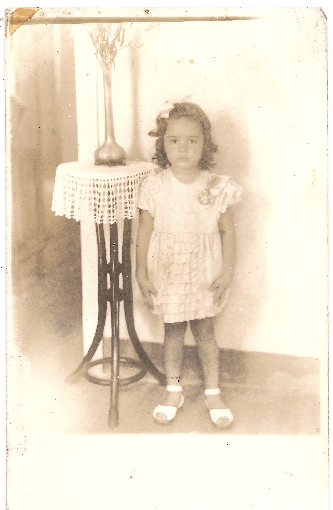 Com 5 aninhos, com vestido cor de rosa com flores e lacinho nos cabelos ruivos, a pequena Bernadette se prepara para a festa, mas antes, uma foto na casa de sua avó perto da mesinha de madeira.