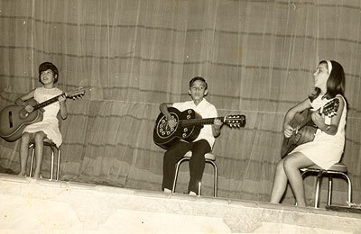 Apresentação de violão de Bebeto no Clube de Três Pontas. Bebeto entre duas meninas, aprendizes de violão.