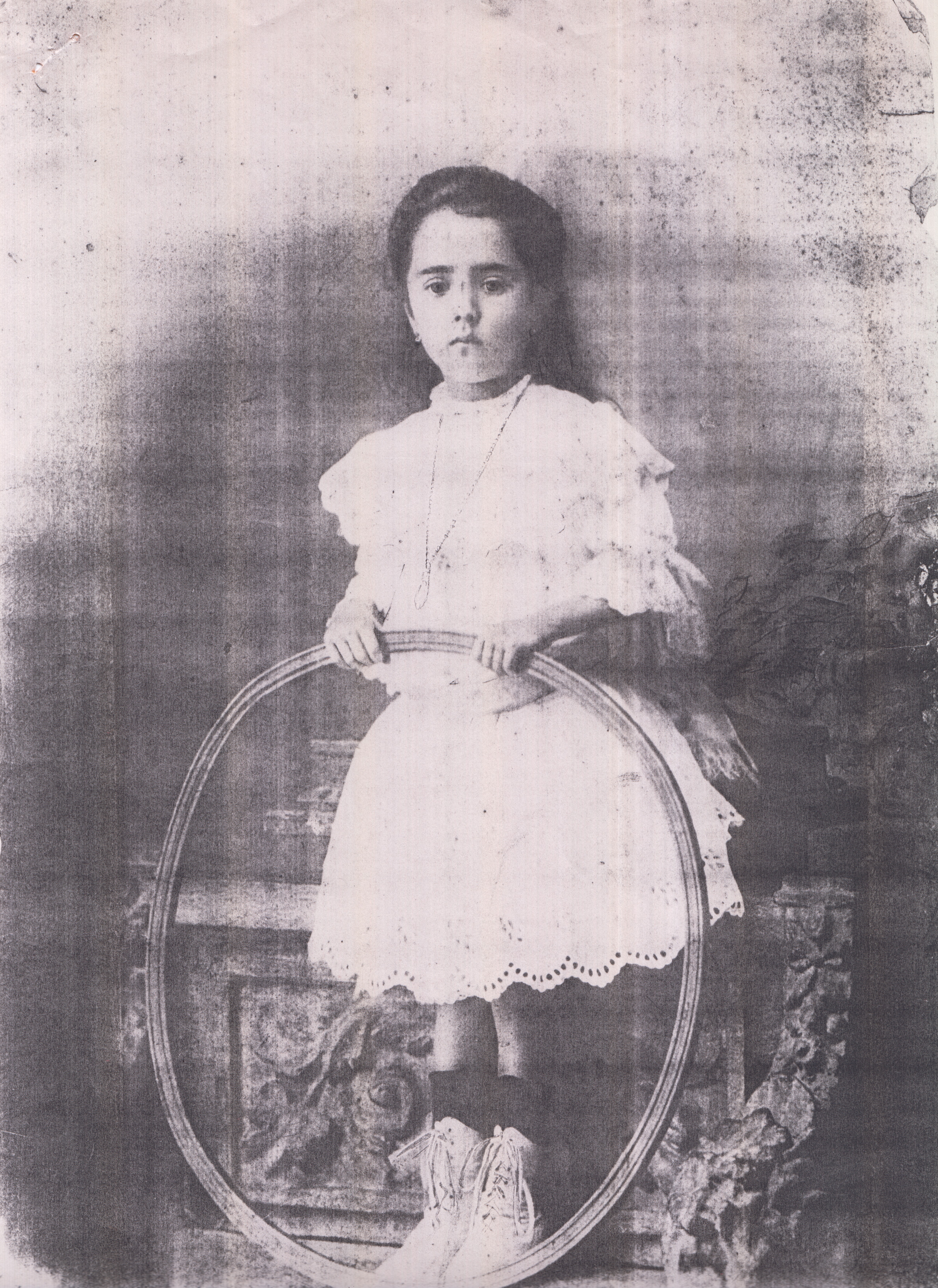 Retrato de Elvira Garrido Borges, tia paterna de Marina, no início do século XX, época onde fazer uma fotografia era um grande acontecimento. Elvira segura um arco, brinquedo que se costumava rodar no chão com a mão ou com um caninho. Era uma época onde não havia muitos brinquedos e os poucos que existiam eram estrangeiros.