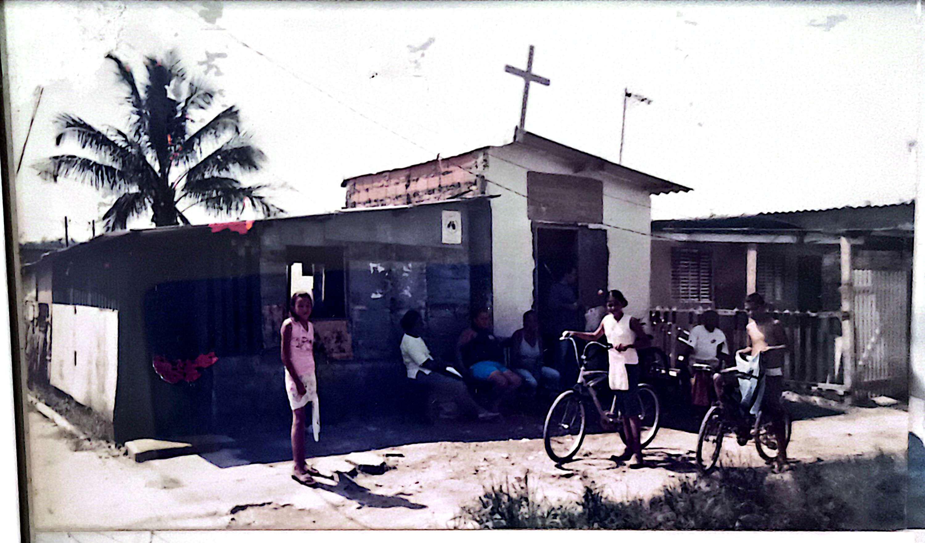 Registro histórico da Igreja Divina Misericórdia, localizada no Ponto Final da Vila Esperança, em Cubatão. A fotografia mostra o templo em sua fase original, construído em madeira, antes das reformas e ampliações que marcaram sua trajetória. Este momento retrata a simplicidade da comunidade e a força da fé que sustentava os moradores da região.