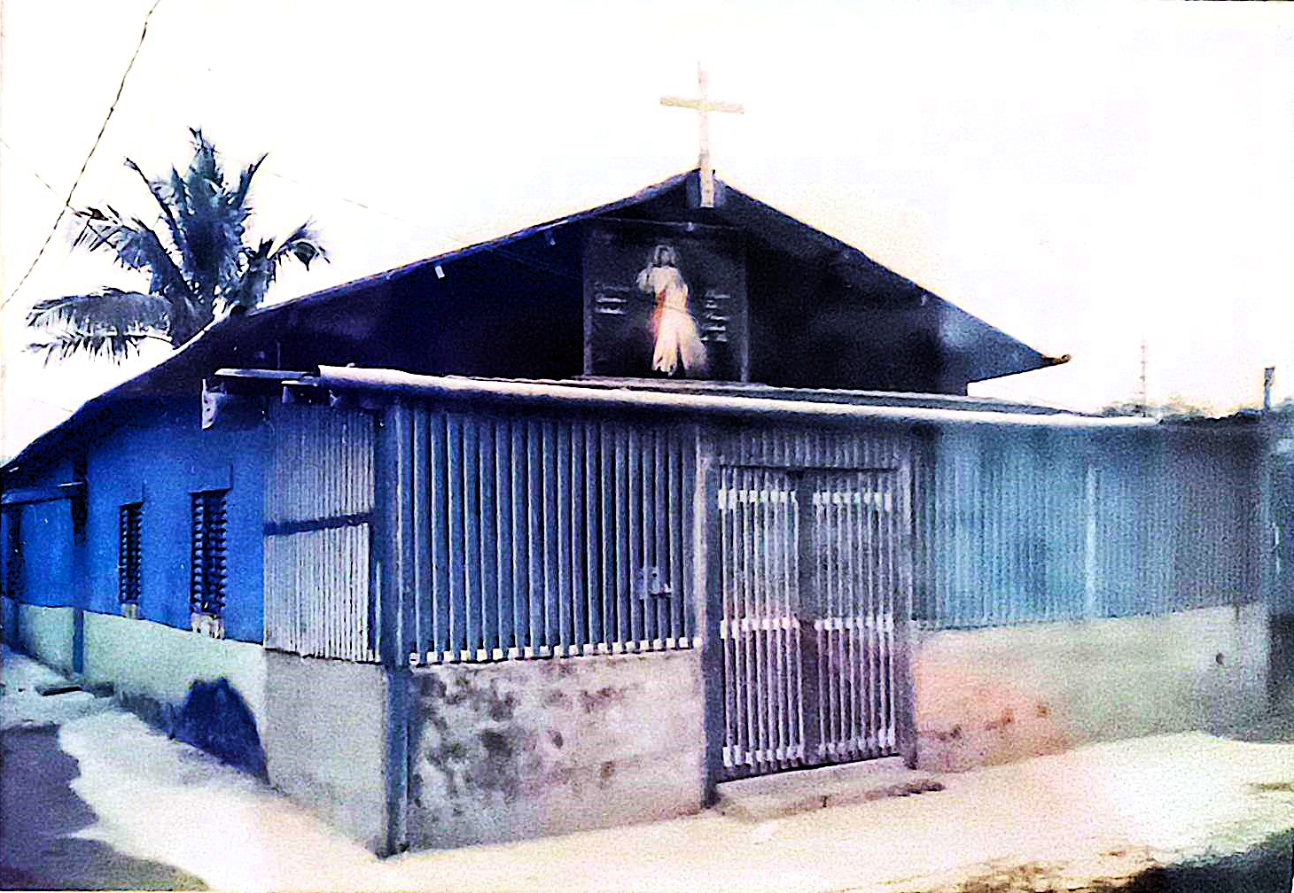 Registro da Igreja da Divina Misericórdia, localizada no Ponto Final da Vila Esperança, em Cubatão, durante o período em que já possuía uma base de concreto, mas mantinha as paredes em madeira. A fotografia evidencia a transição estrutural do templo e a constante necessidade de manutenção.