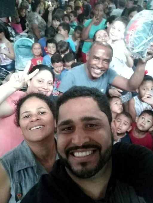 Anderson, Zumbi e Adriana registram em selfie a Festa das Crianças na Associação de Bem com o Mangue, na Vila Esperança, em outubro de 2018. Atrás deles, a alegria toma conta da comunidade: brinquedos distribuídos, festa cheia e muita animação. Uma ação simples, mas poderosa, que aproxima as crianças e fortalece caminhos mais seguros dentro da vila.