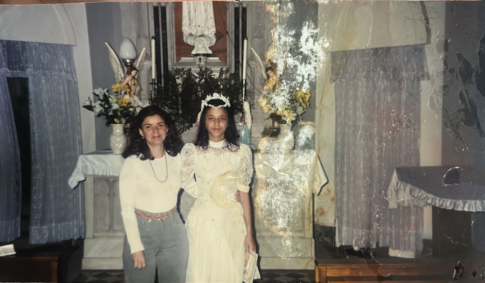 Patrícia, já adolescente, é registrada durante a cerimônia de sua primeira comunhão na Catedral de Santos. A imagem marca um rito de passagem no âmbito da religiosidade católica, acompanhada pela professora de catecismo Fabiana.