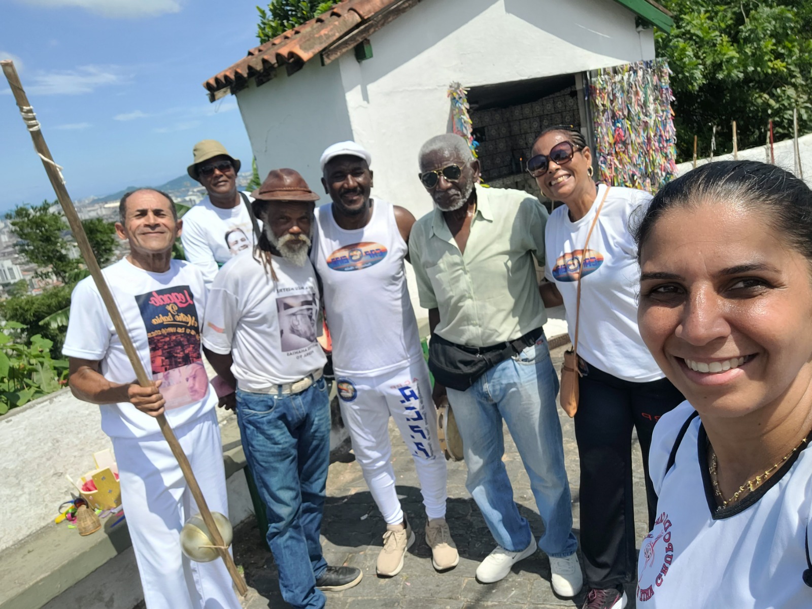 Patrícia aparece ao lado de mestres importantes da capoeira durante a subida ao Monte Serrat, em Santos, no ano de 2024. A imagem foi registrada em um evento em homenagem ao Mestre Bahia e reúne grandes nomes da capoeira, entre eles Mestre Sombra e Mestre Angoleiro. O grupo participa da caminhada como parte da celebração, marcando presença coletiva em um gesto simbólico de respeito e reconhecimento.