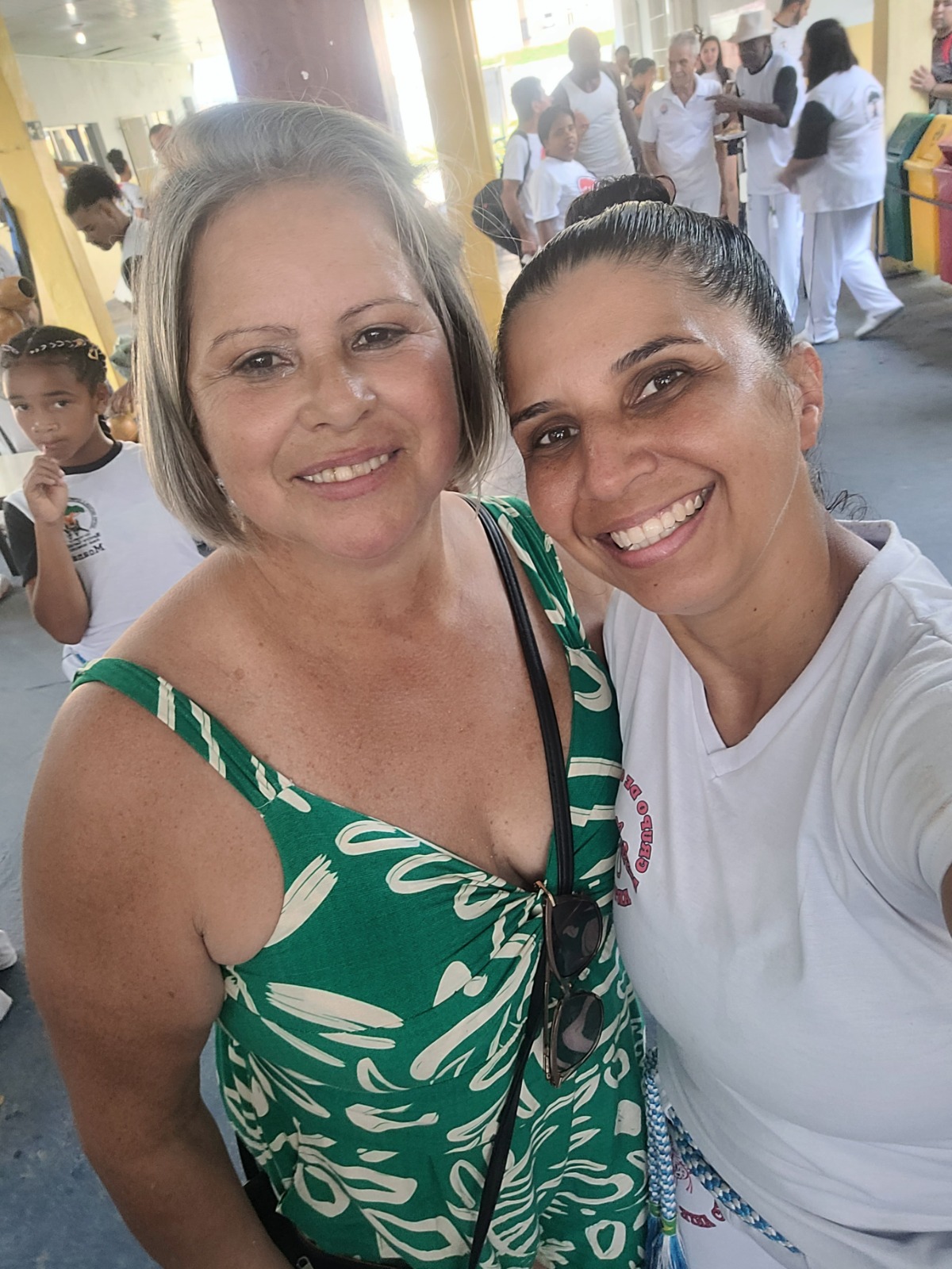 Patrícia aparece ao lado da Professora Márcia, primeira professora de capoeira formada em Cubatão, durante um evento de capoeira. A fotografia foi registrada no evento do Mestre Geraldo e reúne duas mulheres ligadas à trajetória da capoeira na região, em um momento de encontro e reconhecimento mútuo