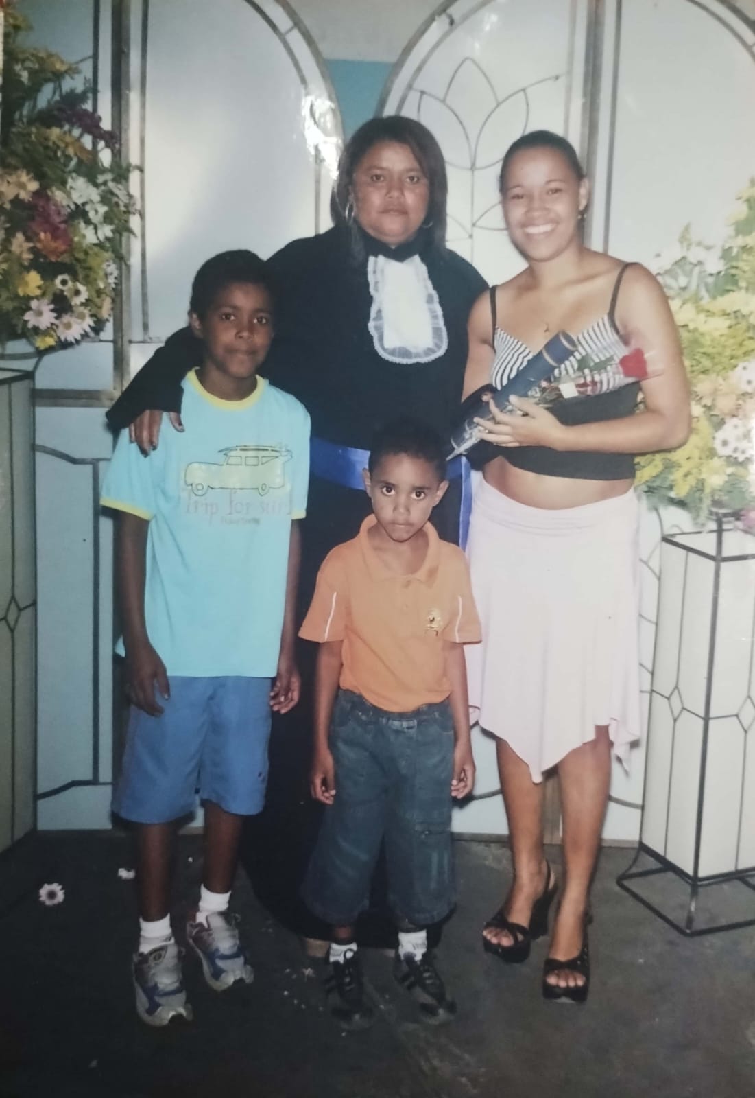 Na formatura de Ivani. A imagem registra o marco simbólico da conclusão dos estudos de Ivani, momento compartilhado com a filha Nayara e os filhos Wallace (à esquerda) e Kennedy (à frente). A conquista acadêmica representa um capítulo significativo de sua trajetória: somente após a estabilização de sua vida em São Paulo foi possível retomar a formação interrompida na juventude, quando, em Petrolina, precisou ingressar no trabalho desde muito cedo.