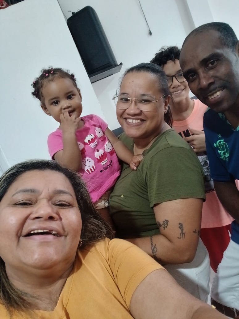 Ivani em selfie com a família reunida em casa. Além dela, aparecem na imagem sua filha Nayara, segurando a sobrinha Maria Lívia no colo; ao fundo, seu filho Davi; e, à direita, o marido Roberto. Ivani relata que costuma receber a neta nos fins de semana, momento que se transforma em verdadeira celebração familiar.
