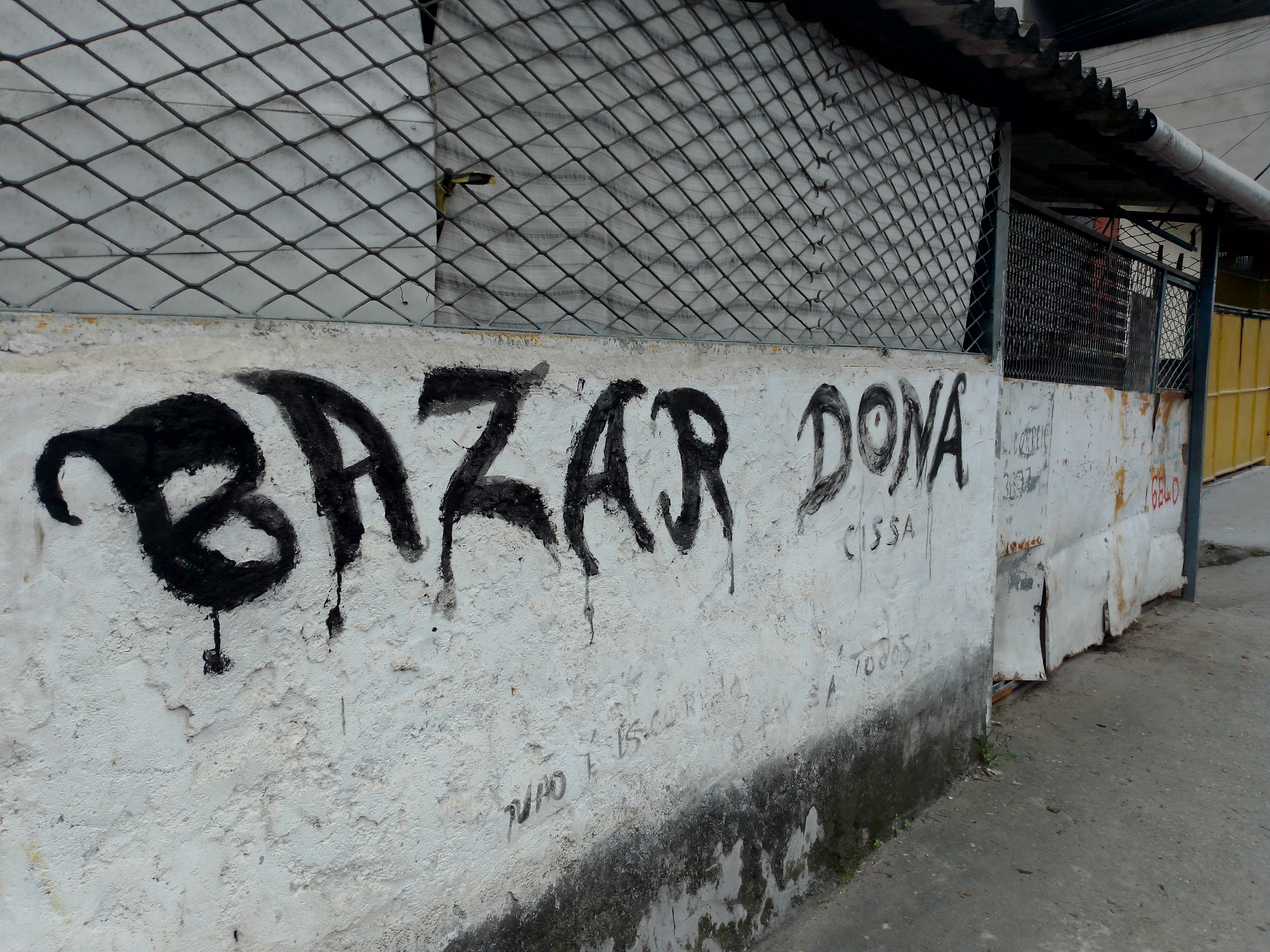 Localizado em frente à casa de Dona Cícera, o Bazar da Cissa foi sua principal fonte de renda nos últimos anos antes de passar a utilizar cadeira de rodas. Por muito tempo, ela manteve o pequeno comércio ativo, cuja fachada ainda exibe o nome do empreendimento, preservando a memória de sua dedicação ao trabalho. Parte das roupas que compunham o estoque ainda estão com ela, como testemunho material dessa trajetória. A imagem retrata um dos aspectos centrais de sua vida: o envolvimento com o comércio local. Nos anos 1990, Dona Cícera também foi proprietária, junto ao então marido Tigrão, do Bar do Forró, um ponto de encontro muito conhecido na Vila Esperança, em Cubatão, que marcou a vida cultural da comunidade.
