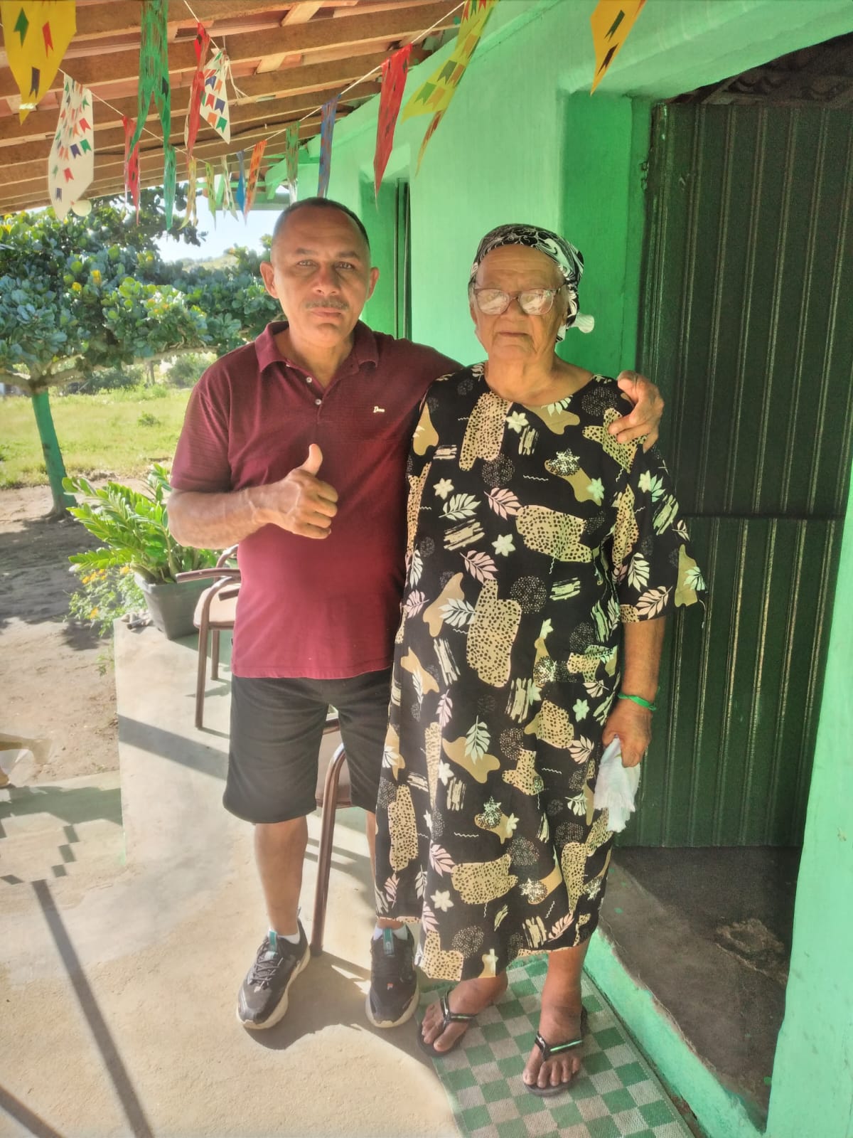A fotografia registra Alfredo em visita à sua mãe, Dona Zefa, no sítio Olho d’Água Cercado, localizado no município de João Alfredo, em Pernambuco, lugar onde ele nasceu, cresceu e onde ela vive até hoje. O reencontro entre mãe e filho é descrito por Alfredo como profundamente emocionante, marcado pela alegria da presença e pela tristeza das despedidas breves, impostas pela vida corrida e pela distância. A imagem revela como o território de origem permanece como referência afetiva fundamental, mesmo após a migração.