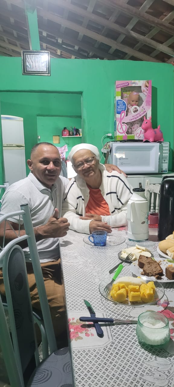 Registro de Alfredo e sua mãe, Dona Zefa, na cozinha do sítio onde ela reside, em João Alfredo, Pernambuco. O ambiente doméstico, com alimentos dispostos, remete à cultura alimentar nordestina que atravessa gerações. A imagem evidencia como os saberes culinários aprendidos nesse espaço familiar acompanham Alfredo ao longo da vida e se manifestam também em seu cotidiano na Vila Esperança, em Cubatão, onde esses sabores são recriados e compartilhados no Cabeça’s Bar. A fotografia conecta memória, afeto e tradição por meio da comida.