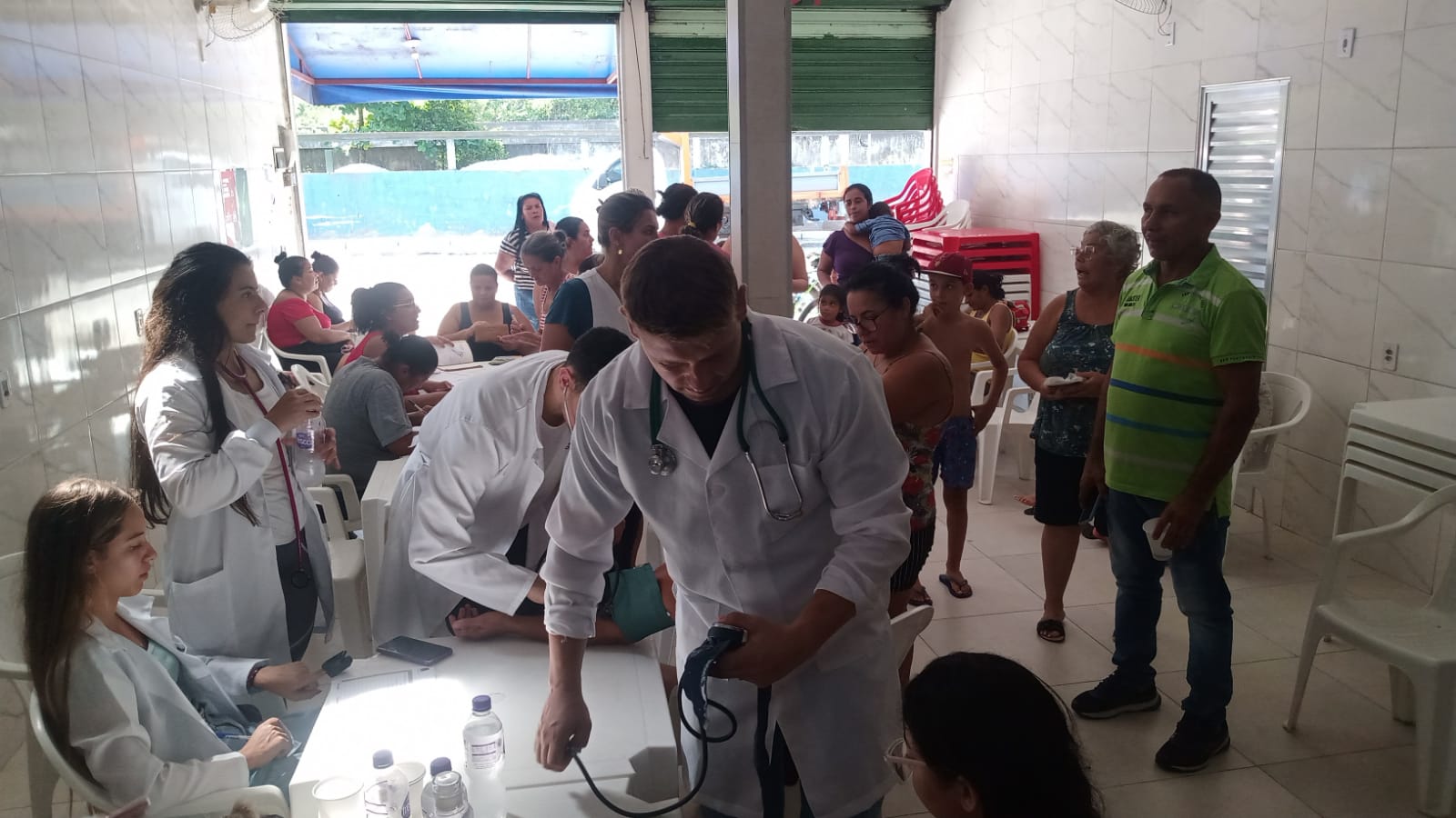 Registro do interior do Cabeça’s Bar durante uma ação de saúde que mobilizou moradores da Vila Esperança. A fotografia mostra o estabelecimento cheio, com atendimentos em andamento, enquanto Alfredo acompanha o funcionamento da iniciativa. A imagem evidencia a adesão da comunidade e a importância de espaços alternativos para suprir a carência de equipamentos públicos de saúde. O bar, temporariamente transformado em ponto de atendimento, simboliza o apoio comunitário e a capacidade de organização coletiva diante das necessidades do território.