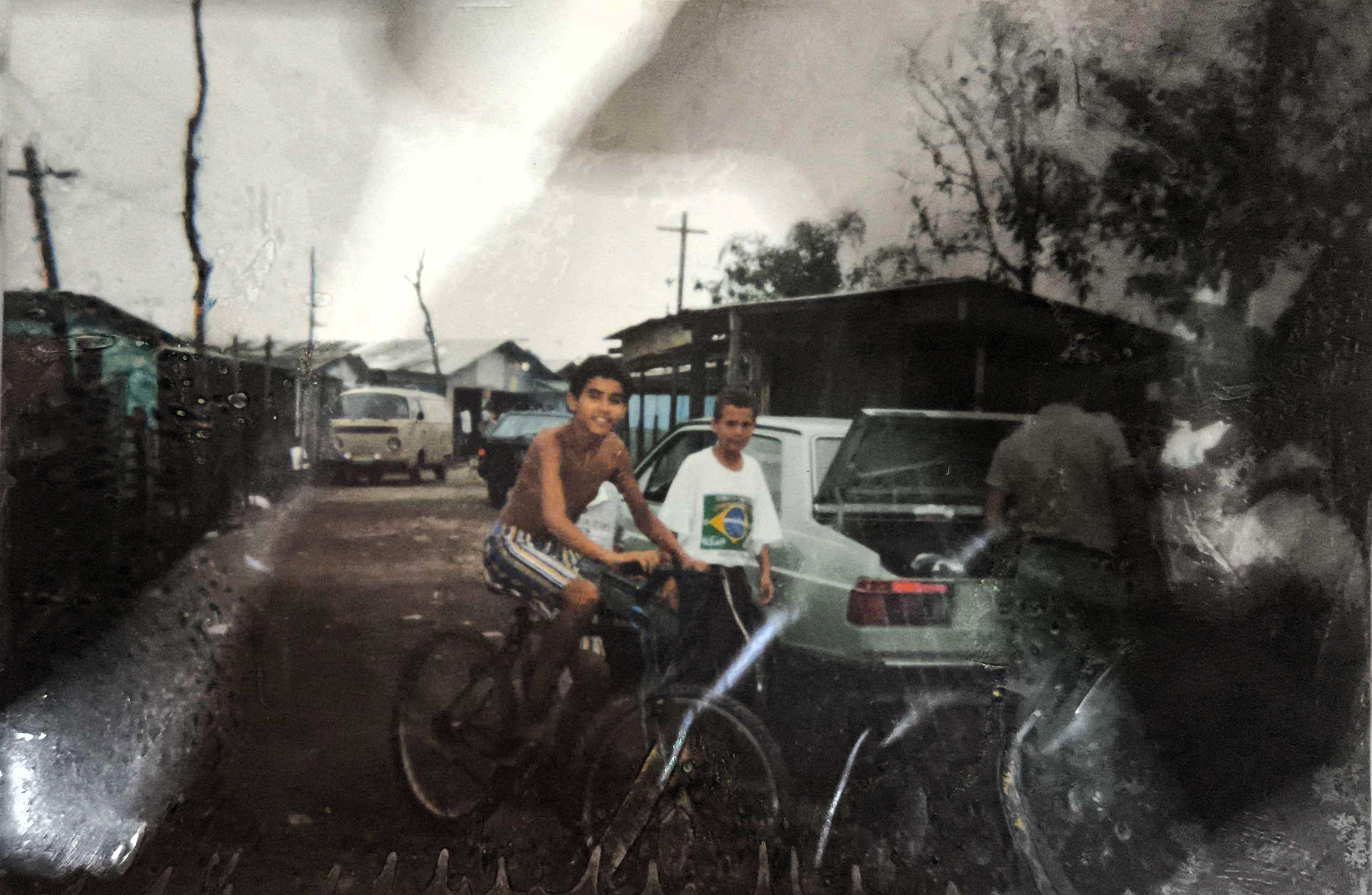 A imagem mostra a parte posterior da Igreja Irmã Dulce, alguns moradores da Ilha Bela e suas ruas. O local, antes sede da Sociedade de Moradores do Jardim Ilha Bela, presidida por Zumbi, foi posteriormente doado por ele para a criação da igreja, num gesto de fé e compromisso coletivo. Após essa doação, a associação se transferiu para a Avenida Principal, onde permanece atuante como a Associação de Educação Ambiental Cubatão De Bem com o Mangue. A fotografia documenta um espaço que carrega memória, espiritualidade e transformação social.