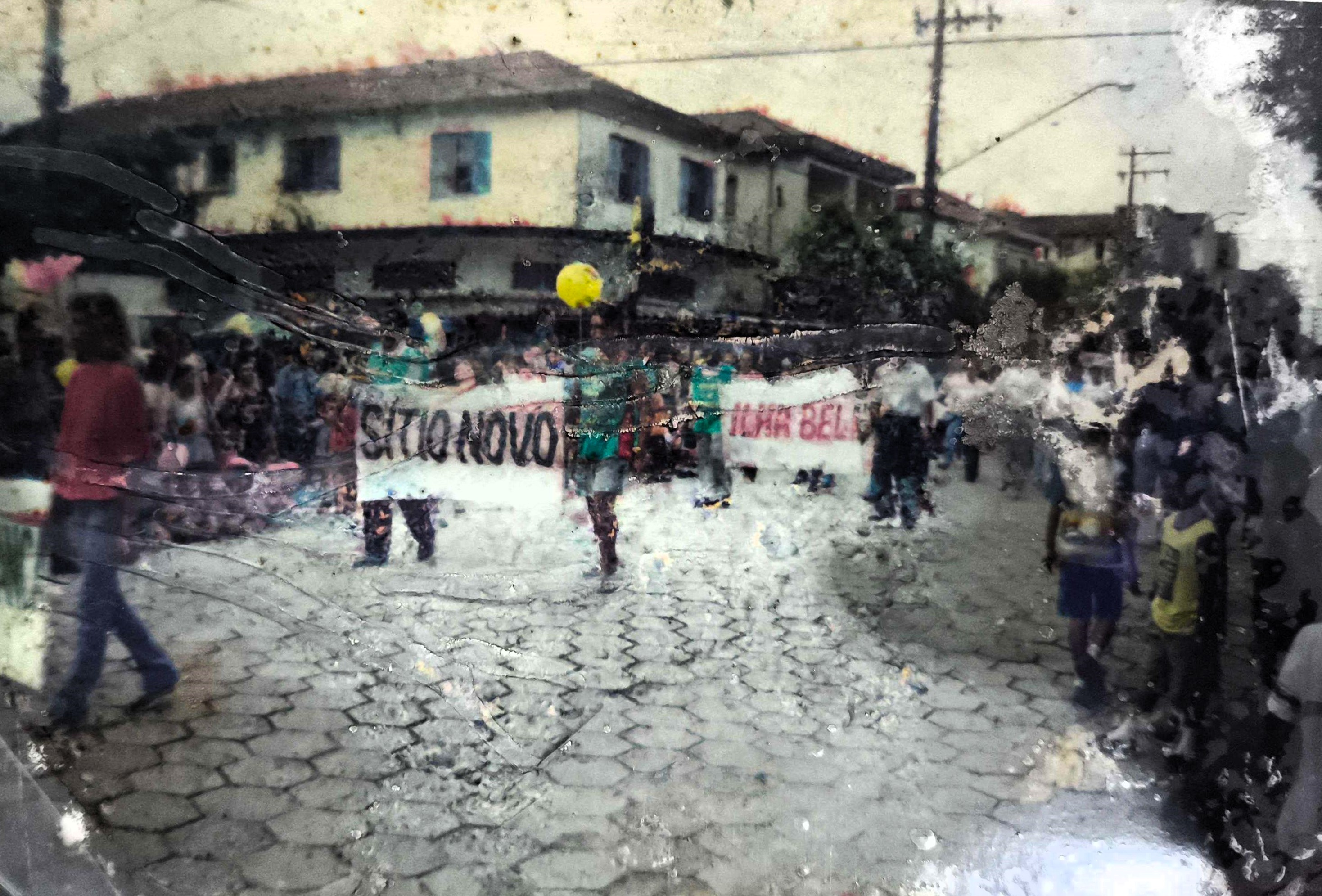 A imagem registra um desfile que apresentava os bairros da Vila Esperança durante um evento oficial na cidade de Cubatão, no início dos anos 2000. Moradores carregam faixas com o nome de cada localidade, afirmando identidade, pertencimento e reivindicando reconhecimento público para suas comunidades.
