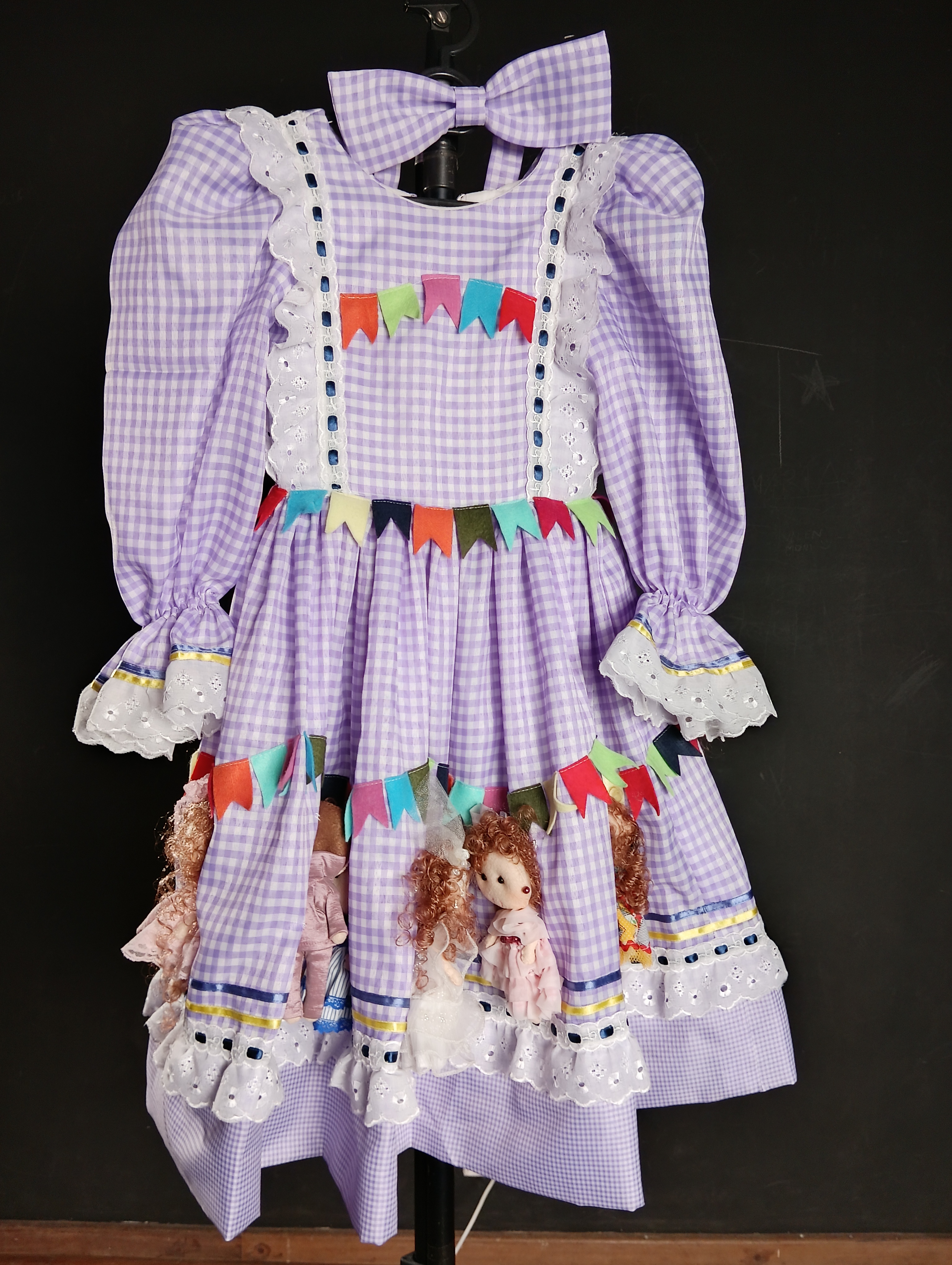 O amor de Marilda por esta data comemorativa é tão grande que ela começou a criar vestidos para este evento. Este vestido foi feito para Lívia dançar a quadrilha na festa junina do colégio EAC. Foi elaborado com 25 bonequinhos de feltro que representam os personagens da quadrilha, como os noivos, os pais dos noivos e as madrinhas amigas. Os bonecos foram bordados em volta de toda a saia do vestido. Marilda fez especialmente para essa ocasião, é uma peça única.