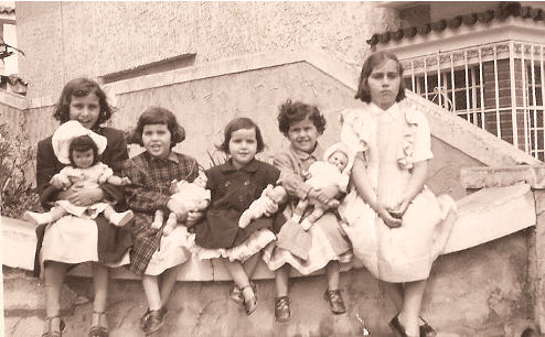 Márcia e suas irmãs sentadas no muro de sua casa no bairro do Ipiranga, durante a infância. Márcia conta que provavelmente Isabel estava emburrada de ter que se sentar no muro, todas, exceto ela, carregavam uma boneca no colo.