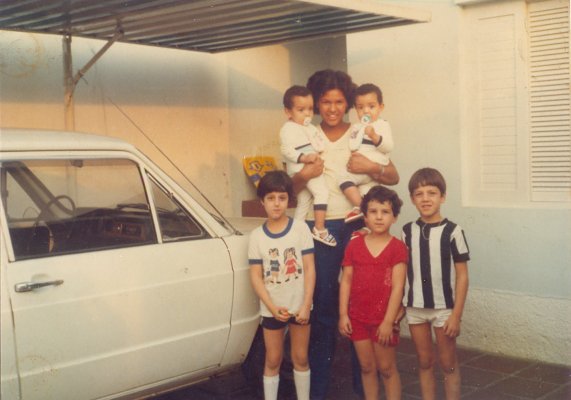 Maria Helena segurando os gêmeos Adilson e Alexandre. Abaixo estão algumas crianças da rua que gostavam de ir à casa de Yara, mãe dos bebês. Yara foi quem tirou esta foto e Maria Helena se recorda de um bolo de chocolate que Yara tinha feito.