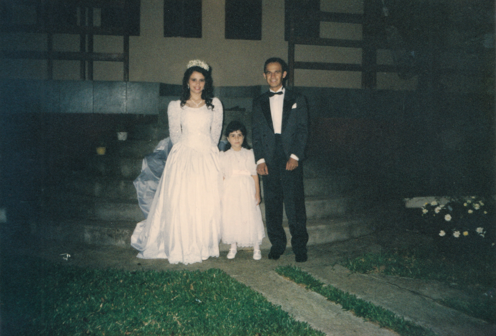 A imagem registra o casamento de Sandra e Vagner, realizado em outubro de 1996, na Igreja Nossa Senhora do Carmo, próxima à estação Capão Redondo, em São Paulo. Na fotografia, aparece também Silvana, prima de Sandra, então com cerca de seis anos. O momento retratado já é da festa, realizada em Itapecerica da Serra, celebrando o início da vida conjugal do casal.
