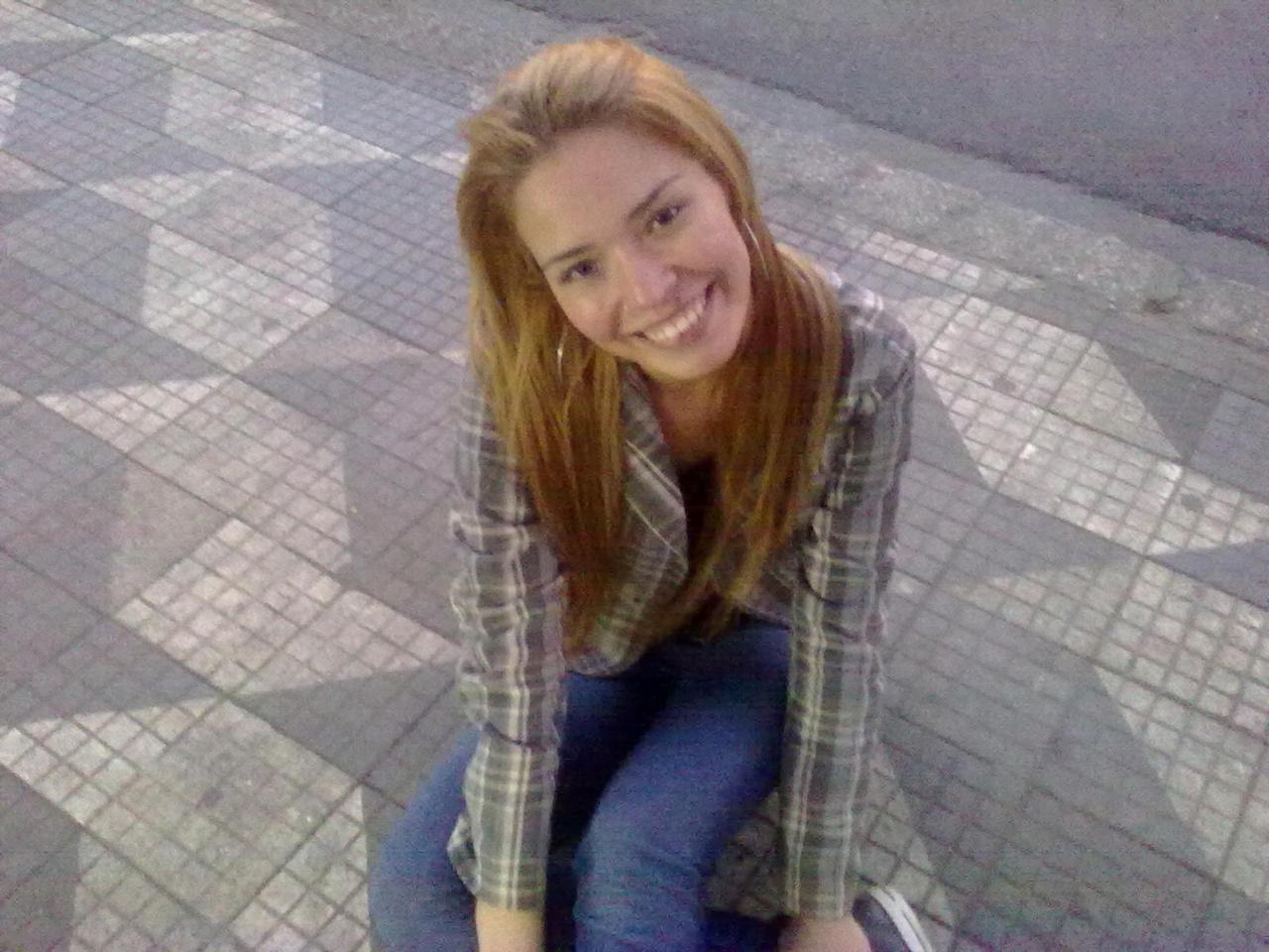 Dayana posa em uma calçada típica da cidade de São Paulo. A imagem associa o espaço urbano ao cultivo de sonhos, revelando a cidade como solo fértil para projetos de vida.