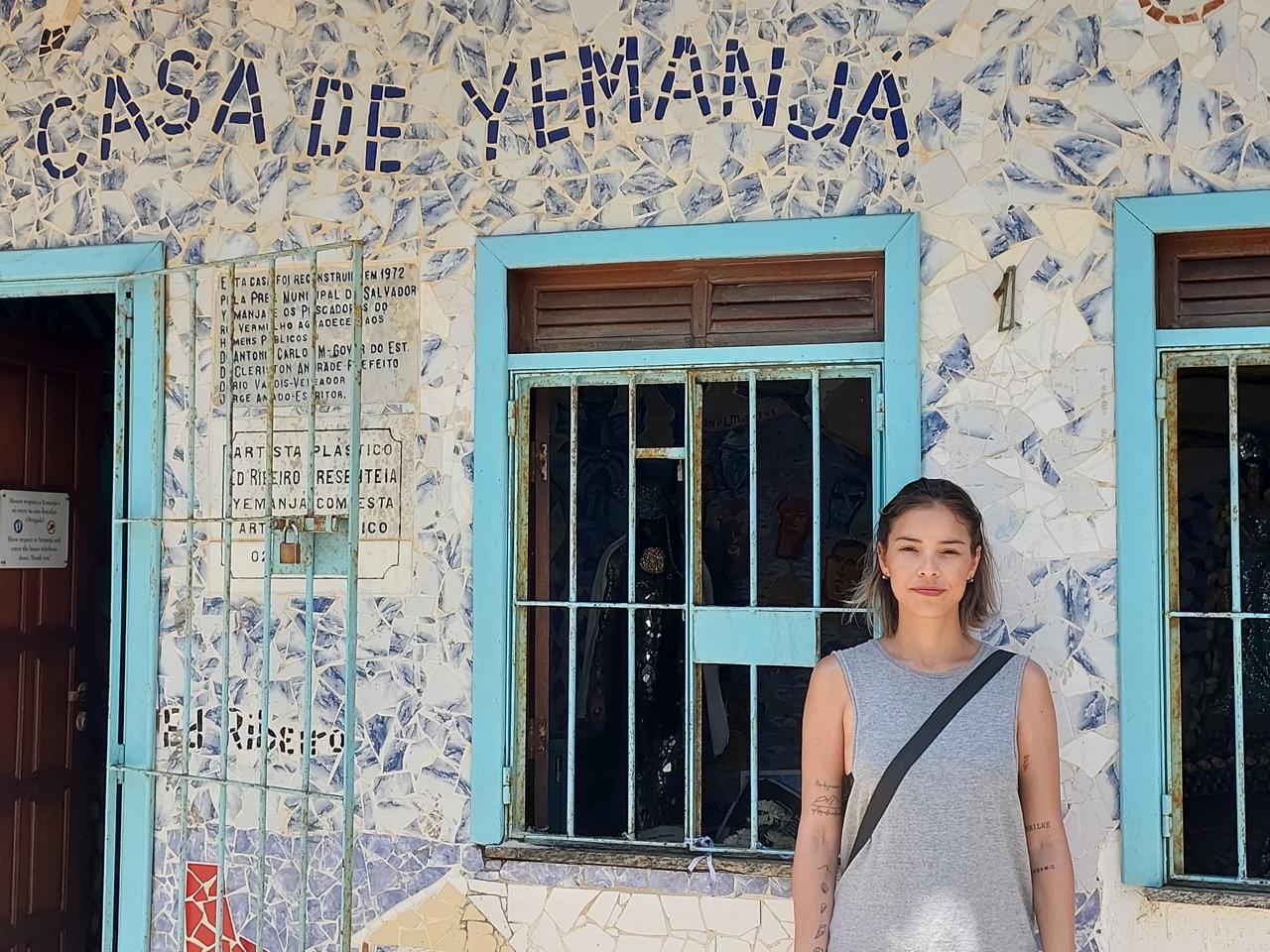 Dayana realiza o sonho de conhecer Salvador e visita a Casa de Yemanjá. A imagem evoca o acolhimento, espiritualidade e a sua memória inesquecível do perfume e da energia do lugar.