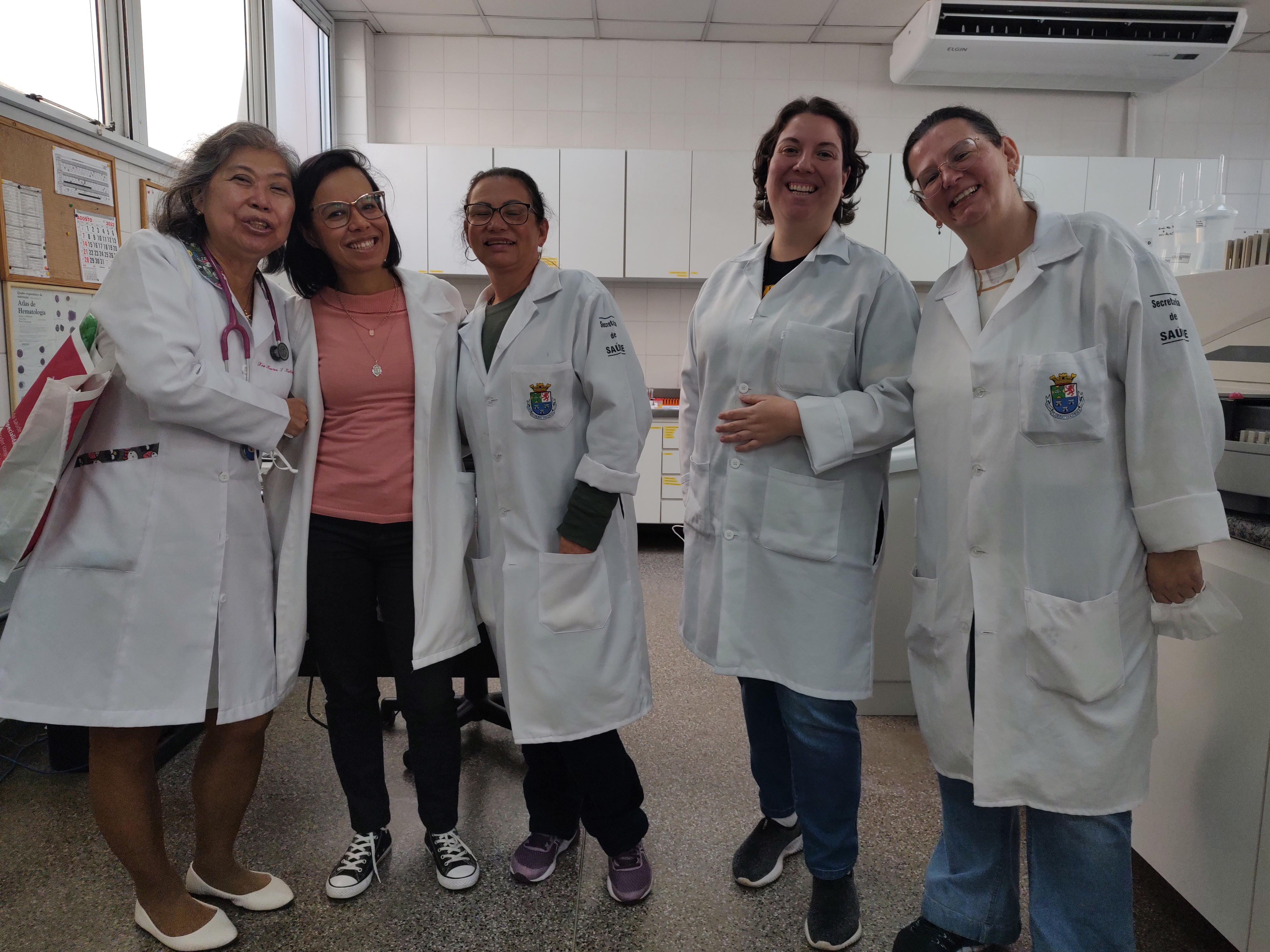 Marina aparece ao lado das funcionárias biomédicas do Laboratório de Exames do Ambulatório Quarteirão da Saúde, em Diadema. O registro marca o período de sua aposentadoria, cercada por colegas prestativas e dedicadas, que fizeram parte de sua trajetória profissional. A fotografia guarda a memória de um ciclo que se encerra, revelando o afeto e o reconhecimento construídos no cotidiano de trabalho e na convivência com a equipe.