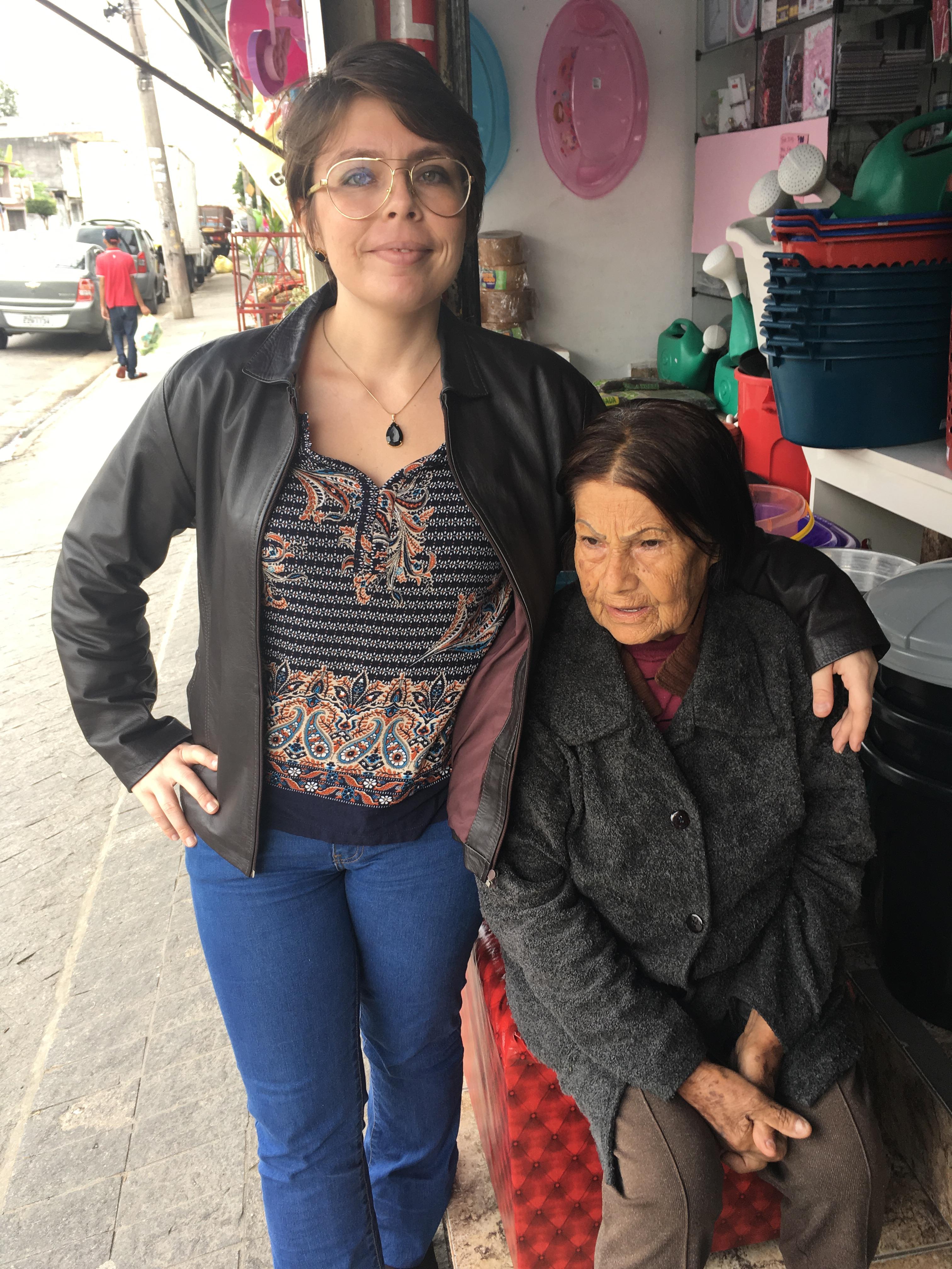 Christiane aparece ao lado de sua avó, Ana, em frente à loja pertencente à sua sogra, localizada na Zona Leste. A fotografia foi registrada alguns meses antes do falecimento da avó e revela a proximidade entre gerações.