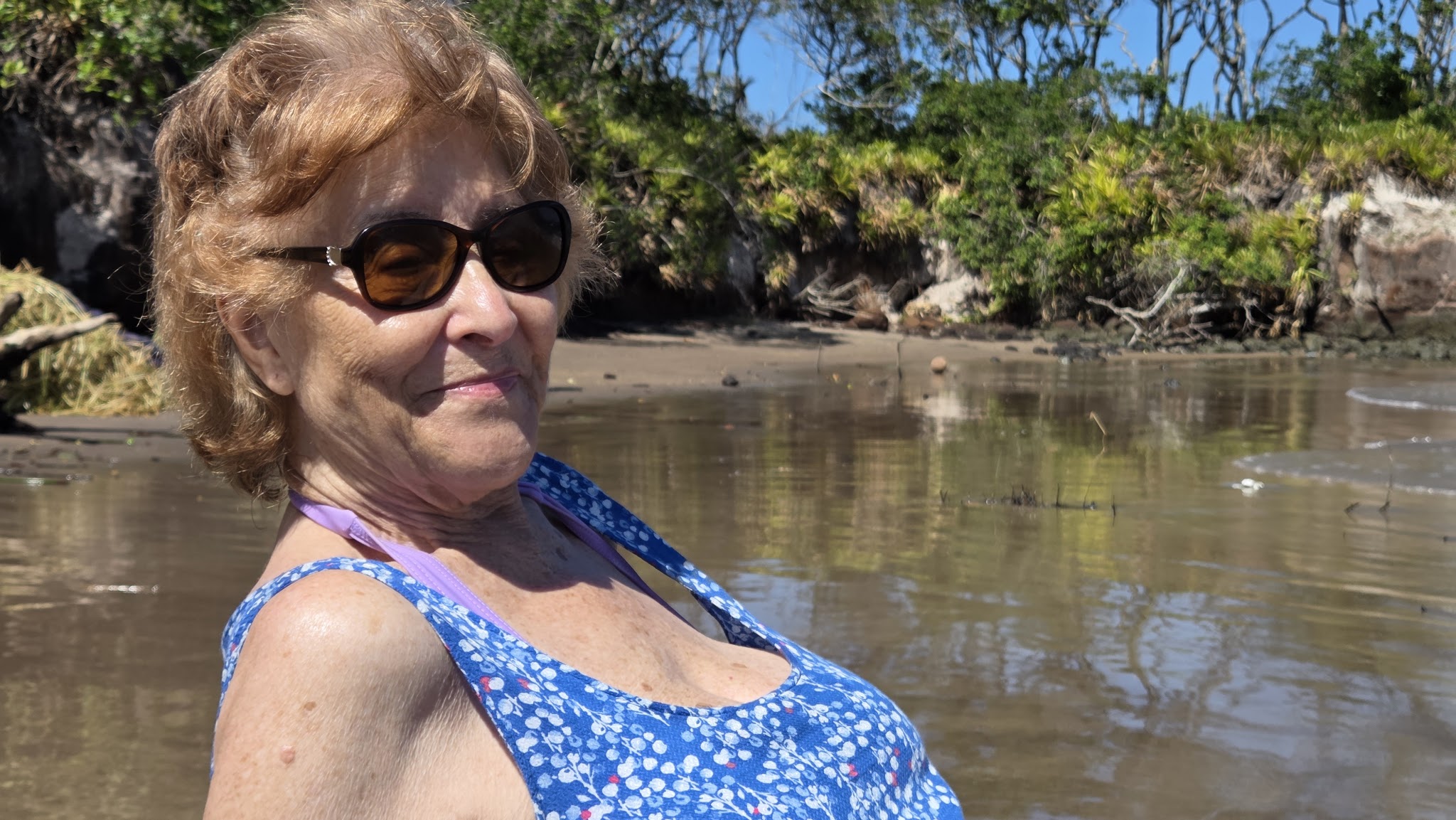 Registro de Antonieta, mãe de Vinicius Pereira de Souza, sorrindo, em uma praia deserta no Brasil.