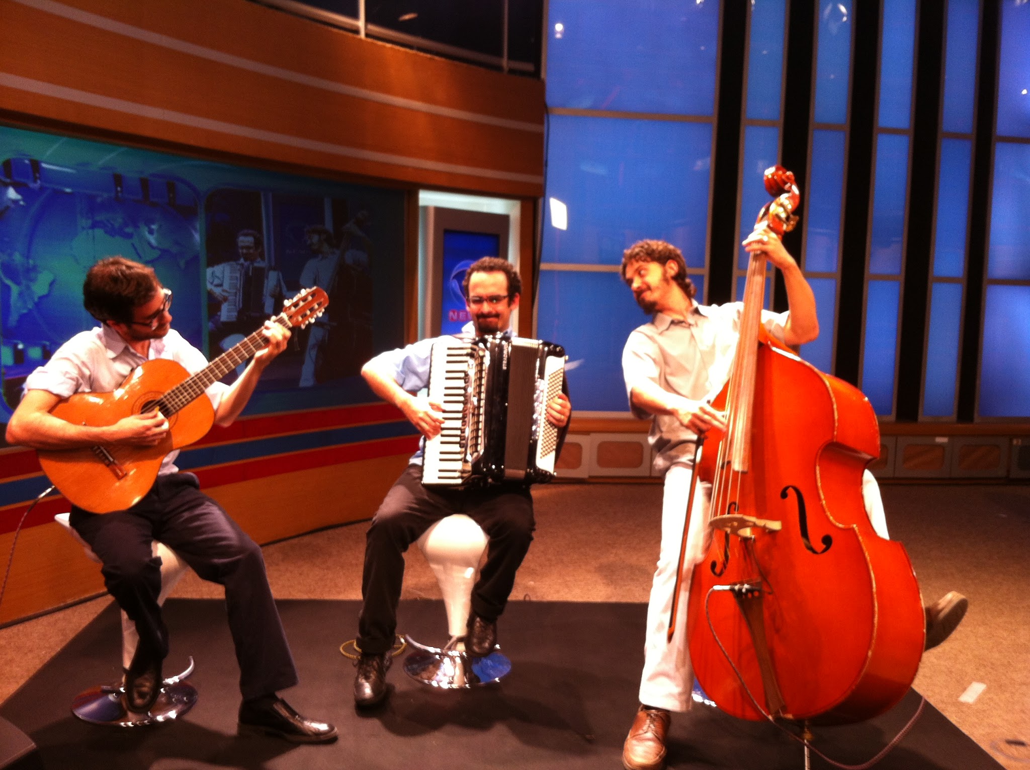 Apresentação ao vivo e entrevista do trio Jogando Tango nos estúdios da Record TV, conduzida pelo jornalista Heródoto Barbeiro. Juan Pablo Ferrero posicionado à esquerda tocando violão, Ricardo Pesce ao centro com o acordeão, e Vinicius Pereira de Souza à direita comandando o contrabaixo.