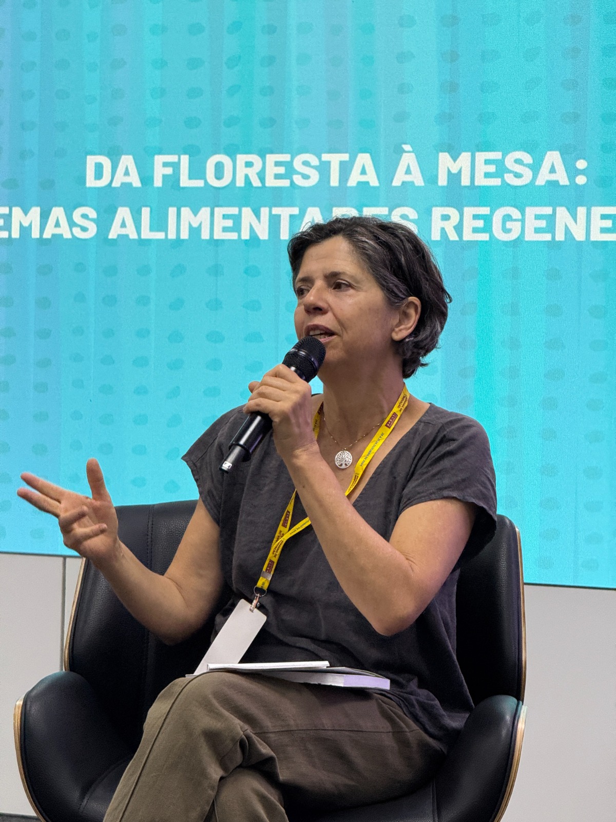 Cláudia Visoni durante uma palestra em Brasília, falando ao microfone sobre sistemas alimentares regenerativos.