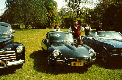 José pousando ao lado de um carro tipo Jaguar, tendo à sua esquerda o automóvel Chevrolet 46 e à direita o modelo Mustang durante exposição de veículos antigos no Grande Hotel São Pedro.