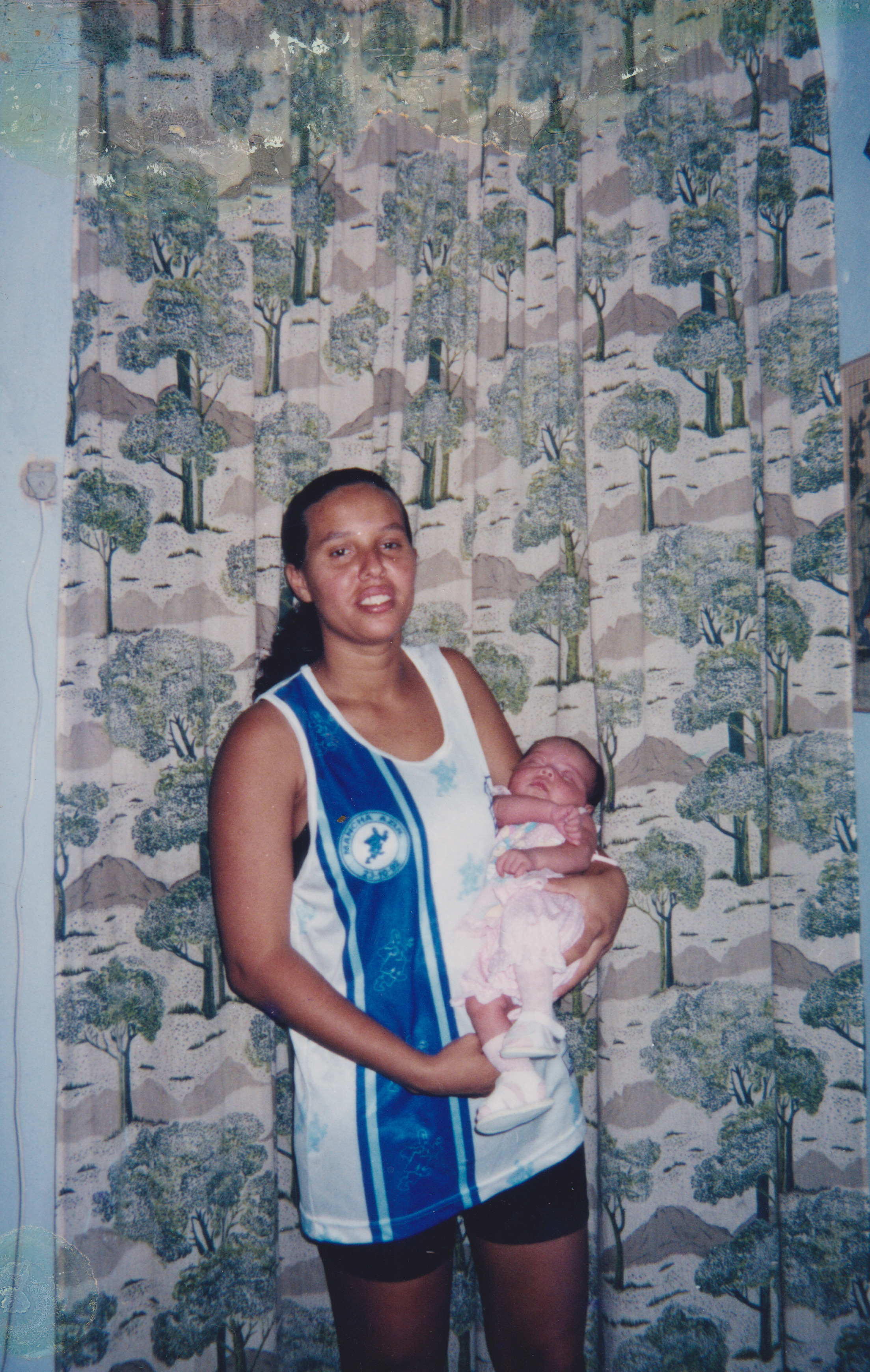 Mãe do ely com sua irmã nos braços com a blusa da mancha azul.