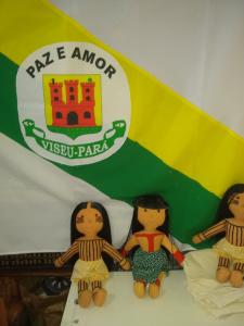 Essa bandeira é do Município de Viseu, Pará, cidade onde Luakam nasceu. As bonecas estão junto à bandeira porque elas dão muito orgulho para os conterrâneos. Uma foto muito importante para Luakam e seu povo, porque os conterrâneos sabem que Viseu está no mundo através das Bonecas Anaty.