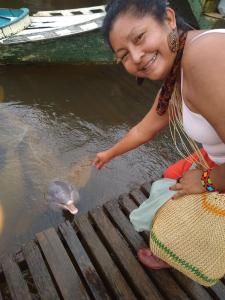 Esta foto foi tirada durante uma viagem que Luakam fez para a aldeia Anambé. Antes de chegar no destino final parou em Mocajuba, um braço do Rio Amazonas, para tomar um Tacacá e ao chegar na margem do rio de Mocajuba ela foi agraciada pela recepção de vários botos-cor-de-rosa do Rio Amazonas. Este foi o seu primeiro contato com botos. 
Esta foto foi tirada durante uma viagem que Luakam fez para a aldeia Anambé. Antes de chegar no destino final parou numa cidade para tomar um Tacacá e ao chegar na margem do rio de Mocajuba ela foi agraciada pela recepção de vários botos-cor-de-rosa do Rio Amazonas. Este foi o seu primeiro contato com botos. 
Há uma lenda no Pará de que o boto é encantado, então esse dia foi muito emocionante para Luakam. Ela também ficou impressionada com a inteligência dos botos. Um parente indígena entrou dentro d'água e fingiu que estava se afogando, então este boto veio rapidinho e entrou debaixo do braço dele e tentou levá-lo para a superfície.