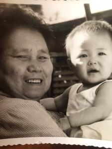 Nesta foto Rosely está no colo de sua avó Kimi. Os avós paternos de Rosely são imigrantes japoneses, saíram do Japão e chegaram ao Brasil para trabalhar nas fazendas de café. Quando pequena, a família de Rosely morava com os avós paternos, então o contato delas era muito próximo na primeira infância. Rosely lembra que quando era pequena passava muito tempo com sua avó, dormiam à tarde e passeavam juntas. À noite sua avó a levava para ver as estrelas no quintal e rezavam para a lua.