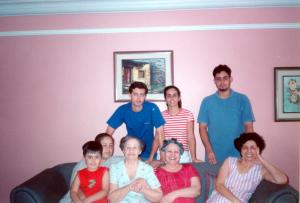 Retrato de Mirna e sua família no sofá. De pé, da esquerda para a direita: Flávio (sobrinho), Danielle (sobrinha e filha adotiva), João Paulo (sobrinho). Sentados: Jean (sobrinho e neto), Elizabeth (irmã), Diva (mãe), Olnei (irmã) e Mirna.