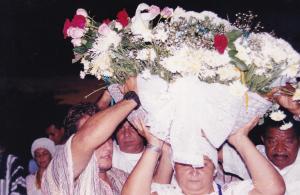 Mãe Néia e sacerdotes na festa de Yemanjá carregando balaio de flores ao anoitecer. Registro na Praia de Camburi, em Vitória?