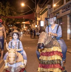 Registro do carnaval de rua de Santa Leopoldina, com Bebeto ao lado de sua neta Juju. Na imagem, os dois participam da festa utilizando mulinhas artesanais confeccionadas por Bebeto, especialmente para que a neta pudesse brincar e se divertir com ele durante o carnaval