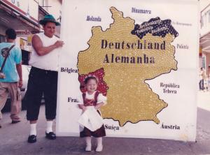 Nínive, criança, no Sommerfest, com seu pai (Rogério de Carvalho). 
Seu pai trabalhava na prefeitura e, para esta celebração, fez o mapa da Alemanha com tampinha de garrafa pet. A foto foi tirada na Avenida Presidente Vargas.