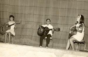 Apresentação de violão de Bebeto no Clube de Três Pontas. Bebeto entre duas meninas, aprendizes de violão.