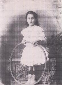 Retrato de Elvira Garrido Borges, tia paterna de Marina, no início do século XX, época onde fazer uma fotografia era um grande acontecimento. Elvira segura um arco, brinquedo que se costumava rodar no chão com a mão ou com um caninho. Era uma época onde não havia muitos brinquedos e os poucos que existiam eram estrangeiros.