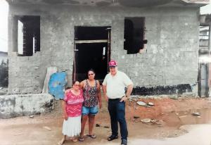 A Igreja da Divina Misericórdia, na Vila Esperança, já com suas paredes erguidas. Em frente à construção, vemos Edite e o falecido Padre Antônio, testemunhando o processo de edificação do templo, que foi sendo levantado pouco a pouco pela força da comunidade.