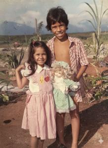 Patrícia aparece ao lado do irmão Fábio de Oliveira Reis, conhecido mais tarde como Mestre Cabrito, em um registro feito na Vila Parisi, local onde viveram durante a infância. A fotografia antecipa trajetórias que se desdobrariam na vida adulta, especialmente a de Fábio, que se tornaria uma referência da capoeira na Vila Esperança, atuando em oficinas, ações culturais e projetos sociais junto à comunidade.