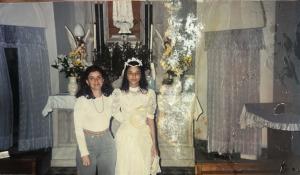 Patrícia, já adolescente, é registrada durante a cerimônia de sua primeira comunhão na Catedral de Santos. A imagem marca um rito de passagem no âmbito da religiosidade católica, acompanhada pela professora de catecismo Fabiana.